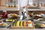 Person using a mandoline slicer to slice vegetables on a kitchen counter.
