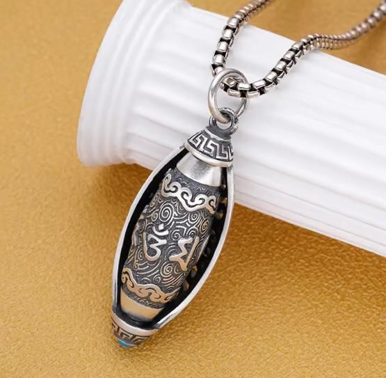 Silver pendant with intricate designs on a white stand against a beige background
